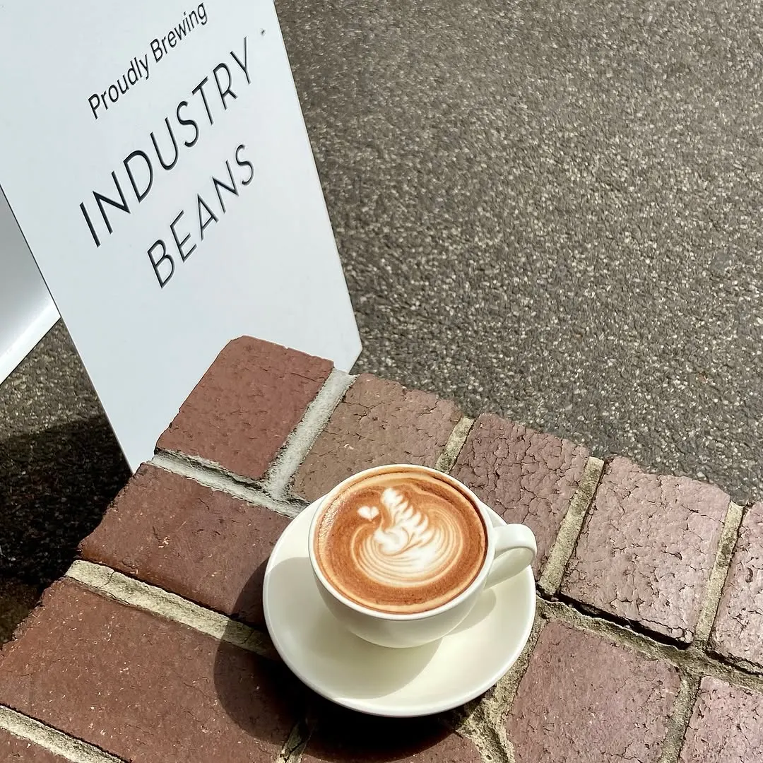 A flat white on brick paving beside an Industry Beans sign
