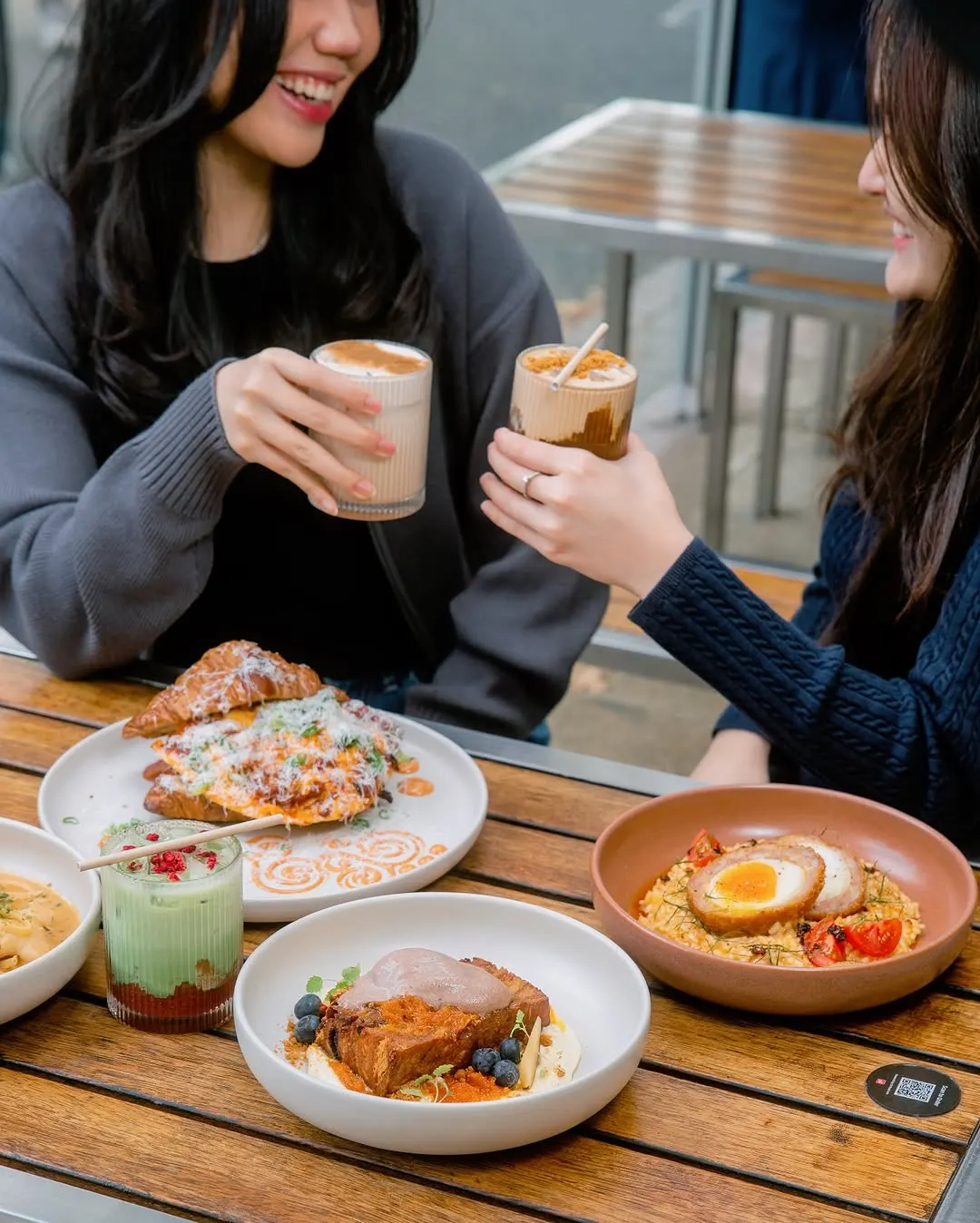 Two friends toasting biscoff cold brews over brunch at an outdoor table